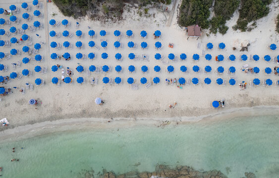 Drone aerial view of Sandy beach with many blue umbrellas and sunbeds. Tourists are relaxing and swimming in the turquoise sea water. Landa Beach Ayia Napa Cyprus