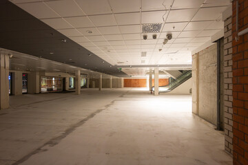 Shopping mall construction site indoors. Empty store without any interiors. Bare floor screed and blank walls. Illuminated hall within the city center.