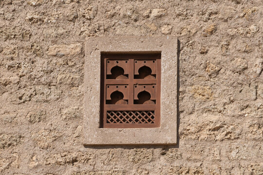 Traditional Omani window with intricate wood carvings and an arched design at Mirbat Castle. Set in a rustic, textured limestone wall, reflecting historic Arabian architecture in Dhofar.