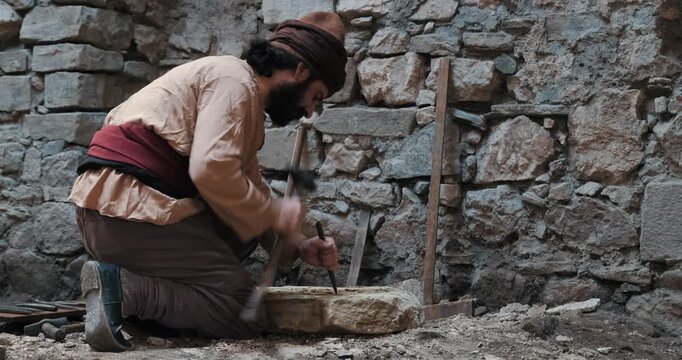 Traditional stonemason carving a rock with a hammer and chisel in an authentic historical setting.