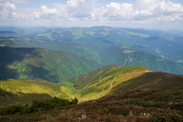 Obraz premium Panoramic view of green mountain ridges and valleys under a partly cloudy summer sky