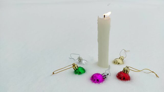 A candle burns in the snow with Christmas decorations