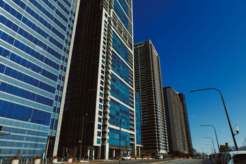 Naklejka premium Tall buildings line the street under a clear blue sky in a busy city scene during daytime hours