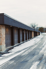 Fototapeta premium Storage units sit along a snowy driveway in winter time at a quiet location near a suburban area