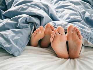 Feet of couple in bed relaxing under blanket