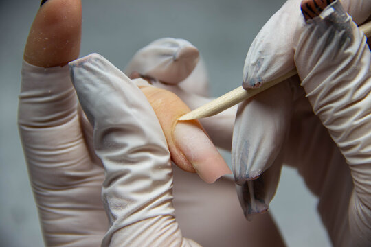 Close-up of a manicured hand with long nails being treated by a technician using a wooden stick for nail care in a beauty salon setting