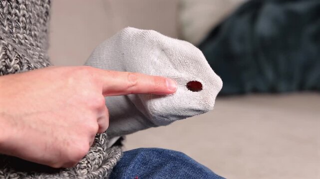 Une personne montrant un trou dans une chaussette avec son doigt, dans le but de la raccommoder.