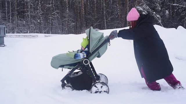 Redhead woman struggling to push baby stroller through deep uncleaned snow on winter road