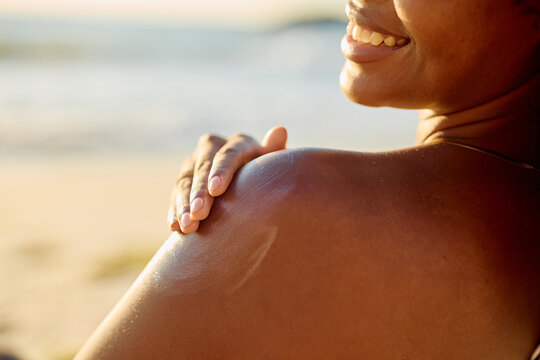 Woman applying sunscreen to her shoulder, protecting skin from sun exposure during a summer day at the beach