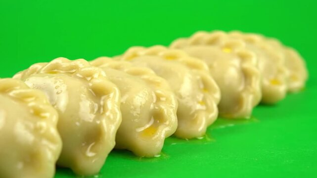 A delectable row of freshly prepared, savory dumplings with a delicate texture, beautifully arranged against a vibrant green background, offering a comforting and traditional culinary experience