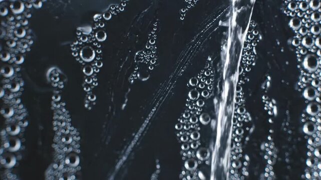 Close-up of water stream flowing over a surface covered in condensation droplets