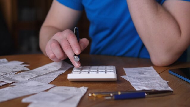 Hands Calculating Tax Totals Among Receipts, Calculator And Pen On Wooden Table, Blue Shirt Sleeve, Busy Scene Of Selfemployed Bookkeeping And Tax Preparation, Focus On Deductions