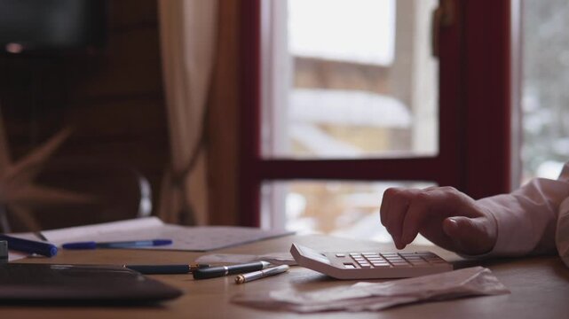 Homeowner Paying Bills. Person Organizing Bills By Window. Individual Managing Expenses In Cozy Workspace Setting. Homeowner Systematically Sorting And Paying Bills Near Snowy Window