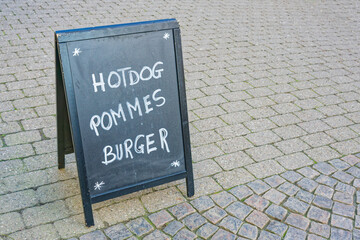 Outdoor chalkboard sign advertising hotdog pommes and burger on pavement