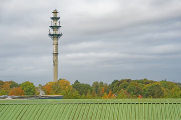 Obraz premium Telecommunication tower standing tall above autumn forest under cloudy sky