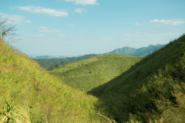 Obraz premium Green mountain valley with rolling hills under blue sky, peaceful natural landscape background with travel and wilderness concept.