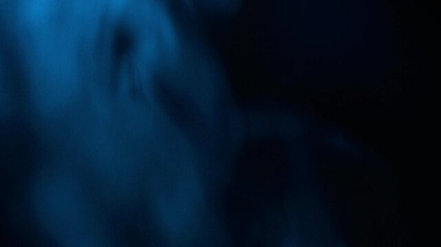 Cinematic abstract shot of ethereal dark blue smoke or vapor swirling and rising against a pitch black background with visible grainy texture and soft atmospheric lighting