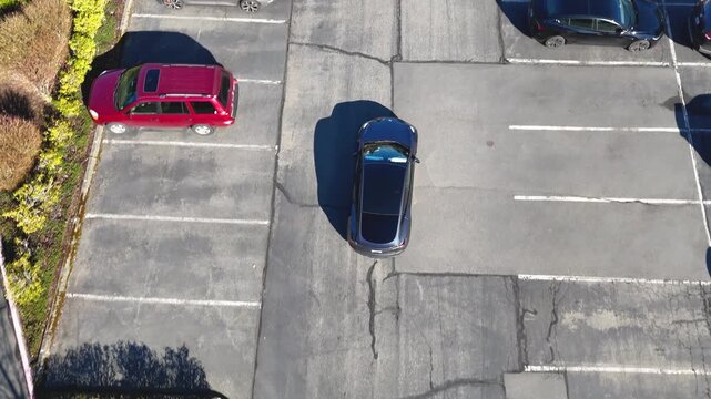 Aerial drone follow shot of a car backing into a parking space in a suburban lot