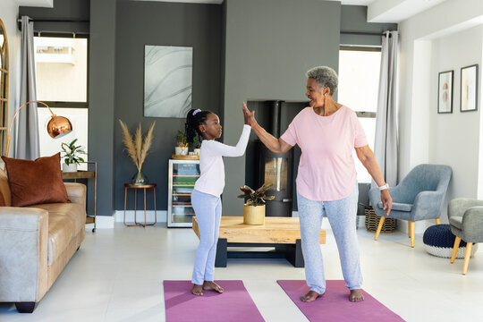 African American female child and senior holding hands on purple yoga mats at home in activewear