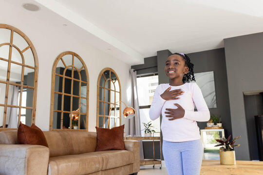 African child standing at home near sofa hands on chest, abdomen wearing pink top, copy space