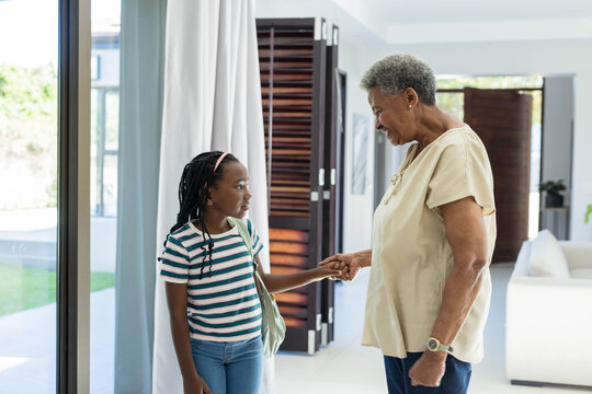 African American senior woman and girl holding hands near glass doors with shoulder bag and watch