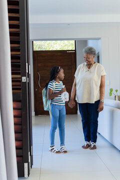 African American senior woman and girl standing, holding hands, child wearing mint-green backpack