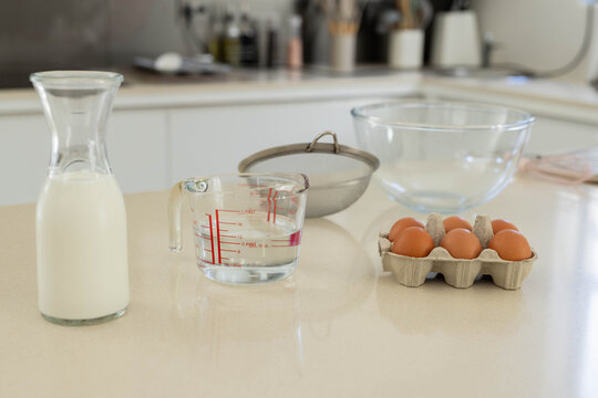 Measuring cup is holding clear liquid and sitting on light countertop with carafe left, eggs right