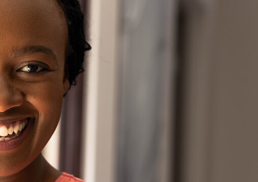 Left half of smiling face catching soft side light near window with coral pink top