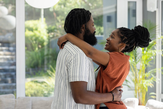 African couple embracing and standing near large glass windows wearing rust top and striped shirt
