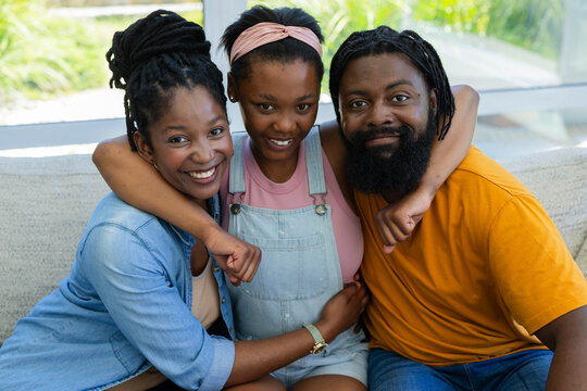 African family with teenage daughter sitting on light couch, smiling and wearing pink headband