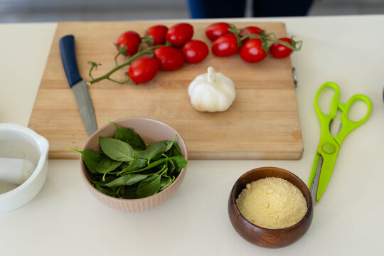 Wooden cutting board is holding vine tomatoes and garlic on countertop, with chef's knife, basil