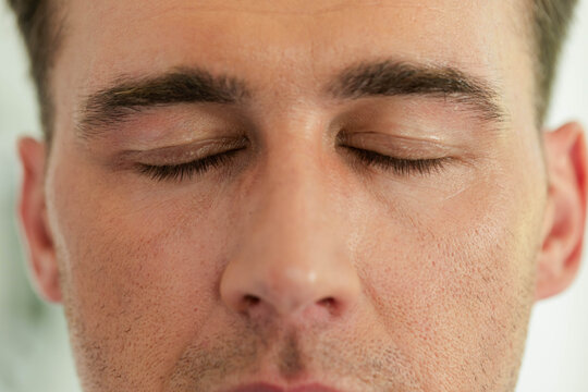 Male resting with closed eyes in softly lit studio, showing stubble pores and eyelashes