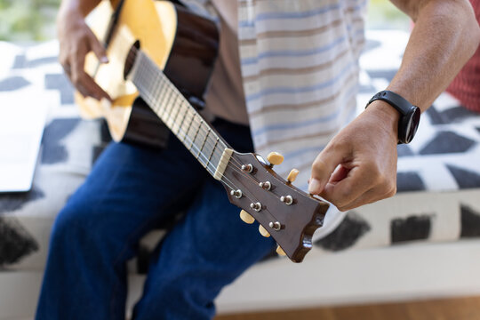 Acoustic guitar being tuned on patterned bench near sunlit window, natural light on headstock