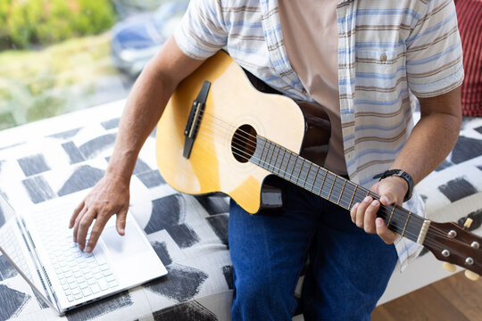 Acoustic guitar resting across patterned sofa cushion with open laptop near window in daylight