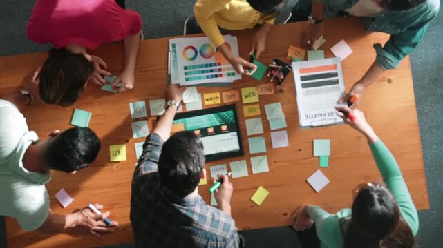 Top view of business people working together to design web design. Aerial view of designer brainstorming and discussing about website interface and looking at tablet with digital design. Symposium.