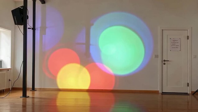Colorful light projections dance on a white wall in an empty room, creating a vibrant and dynamic visual display.