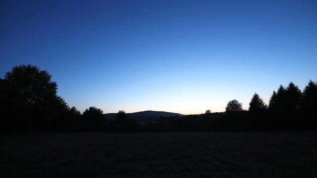 Serene landscape silhouette trees against vibrant sunset sky gradient blue orange hues mountain