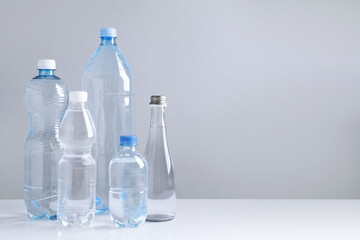 Naklejka premium Water bottles of different sizes on white table against grey background, space for text