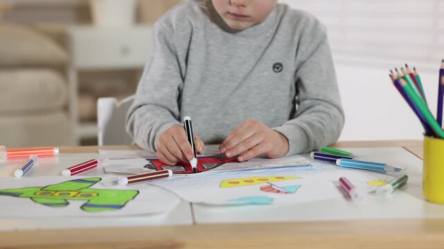 Little boy drawing car with felt tip pen at wooden table indoors, closeup