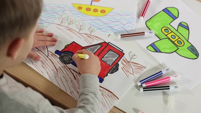 Little boy drawing car with felt tip pen at wooden table indoors, closeup