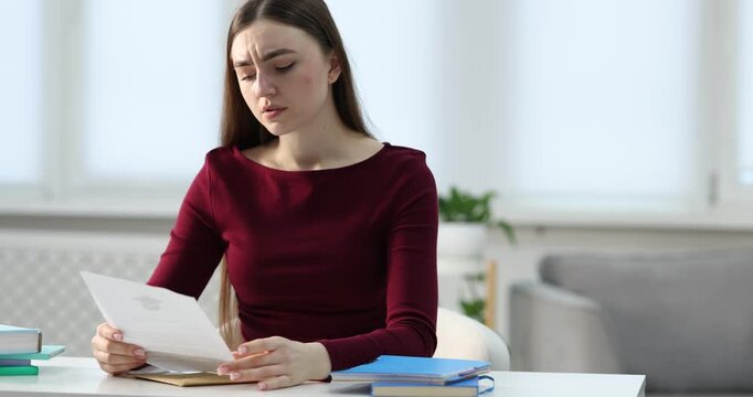 Upset woman reading rejection letter from university at table indoors