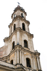 Fototapeta premium Baroque bell tower of the Church of the Blessed Virgin Mary of Consolation in Vilnius, Lithuania, showcasing historic architecture, ornate details, and aged facade against a bright sky.