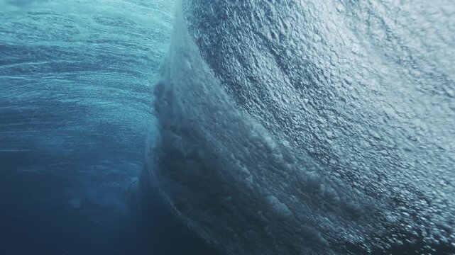 Underwater wave face with textured surface and rolling motion in deep blue ocean water
