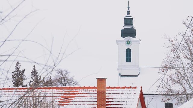 Nemesn&aacute;dudvar church tower with a clock and snowy roofs in Hungary on winter day