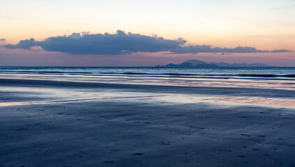 Obraz premium Tropical beach at Koh Tarutao, Ao Son Beach, Thailand. Sunrise over the Andaman Sea. Wide sandy shore and calm ocean waves. Cloudy sky with soft morning light.