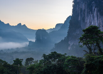Obraz premium Misty mountains in Khlong Phanom National Park at sunrise. Lush green forest with foggy landscape. Tropical jungle in Thailand during morning light.