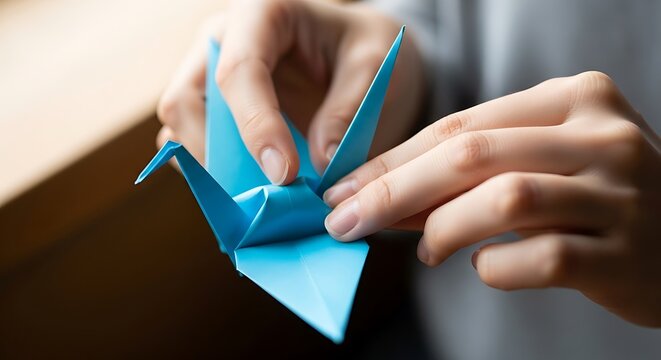 A person creating a bright blue origami crane with bare hands detail
