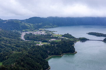 Obraz premium Sete Cidades volcanic lake surrounded by lush green hills. View from Miradouro da Vista do Rei, Sao Miguel Island, Azores, Portugal. Calm water and cloudy sky in the background.