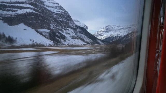Scenic Train Journey Through Snow-Covered Mountains and Reflective Lake Landscape.