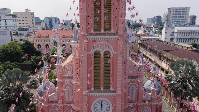 Aerial drone view of the iconic pink church in Ho Chi Minh City, Vietnam. Historic cathedral architecture surrounded by dense urban skyline and modern city buildings.